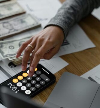 Persona sosteniendo un teléfono inteligente y billetes en la mano, representando planificación y ahorro de dinero para viajes.