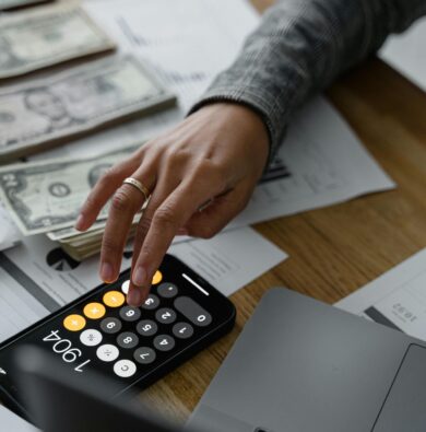 Persona sosteniendo un teléfono inteligente y billetes en la mano, representando planificación y ahorro de dinero para viajes.