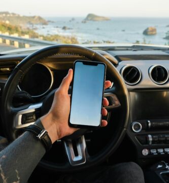 Hombre usando smartphone dentro de su coche junto al mar, gestionando seguro coche digital de manera online